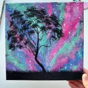 Peut inclure: Une peinture d'un arbre en silhouette sur fond de galaxie color&eacute;e. Le ciel est peint dans des tons de rose, violet, bleu et vert avec des &eacute;toiles blanches &eacute;parpill&eacute;es.