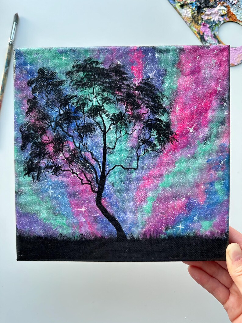 Peut inclure: Une peinture d'un arbre en silhouette sur fond de galaxie color&eacute;e. Le ciel est peint dans des tons de rose, violet, bleu et vert avec des &eacute;toiles blanches &eacute;parpill&eacute;es.