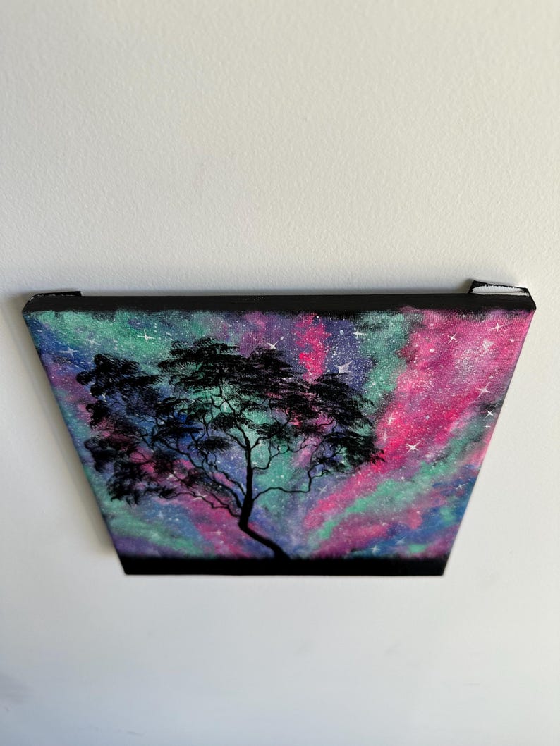 Peut inclure: Une peinture repr&eacute;sentant un arbre en silhouette sur fond de galaxie color&eacute;e. La galaxie est peinte dans des tons de rose, vert et bleu avec des &eacute;toiles blanches.