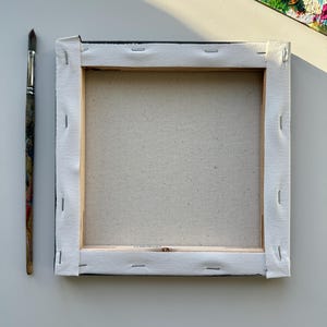 Peut inclure: Une toile blanche tendue sur un cadre en bois avec du ruban adh&eacute;sif noir autour des bords. La toile est vierge et pr&ecirc;te &agrave; &ecirc;tre peinte.
