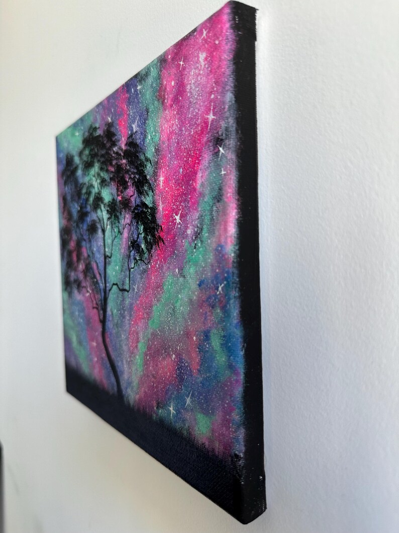Peut inclure: Une peinture repr&eacute;sentant la silhouette d'un arbre devant une galaxie color&eacute;e aux teintes roses, vertes et bleues. La galaxie est parsem&eacute;e d'&eacute;toiles blanches.