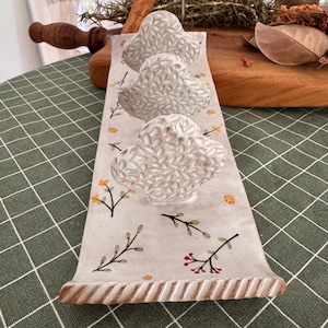 May include: A long, rectangular ceramic tray with a cream-coloured base featuring hand-painted sprigs of small yellow flowers and red berries. Three raised, textured, cloud-shaped ceramic elements are attached in a row along the centre.