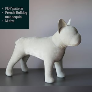 Może przedstawiać: Jasnoszary manekin buldoga francuskiego w rozmiarze M. Pluszowy pies ma zaokrągloną głowę, proste uszy i krótki ogon. Manekin stoi na ciemnoszarej powierzchni. Tekst po lewej: PDF pattern, French Bulldog mannequin, rozmiar M.