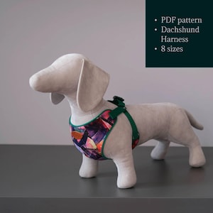 May include: A dog harness with a geometric, multi-colored pattern in shades of purple, orange, and black, featuring green trim and straps. The harness is displayed on a light-colored dachshund mannequin. Text reads: PDF pattern, Dachshund Harness, 8 sizes.
