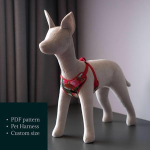 Peut inclure: Un harnais pour chien à motif rouge et vert avec des sangles réglables. Le harnais est sur un mannequin de chien gris.