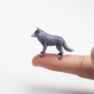 Op de afbeelding: Een miniatuur grijze wolf-figuur met gedetailleerde vachttextuur, puntige oren en een bossige staart. Het kleine diermodel is afgebeeld in een staande positie, met realistische schaduwen en een compacte vorm voor verzamelaars.