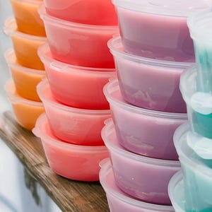 May include: A stack of clear plastic containers filled with colourful wax melts. The wax melts are in shades of orange, pink, and purple.
