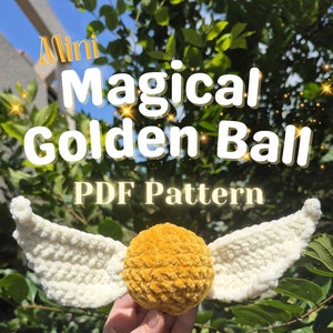 Puede incluir: Una bola dorada tejida a ganchillo con alas blancas, que se asemeja a una Snitch. El texto "Mini Magical Golden Ball PDF Pattern" se muestra encima de la bola. El fondo presenta follaje verde y un cielo brillante.