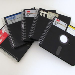 May include: A selection of black spiral-bound notebooks, designed to look like floppy disks. Labels on the notebooks include text such as "Managing Your Money" and "3M High Density." The notebooks are displayed on a white surface.