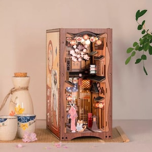 Könnte beinhalten: Ein 3D-Modell aus Holz einer japanischen Straßenszene mit Kirschblüten, Laternen und einer Frau in einem Kimono, die mit einem Hund spazieren geht. Das Modell ist von innen beleuchtet und hat ein detailliertes Interieur.
