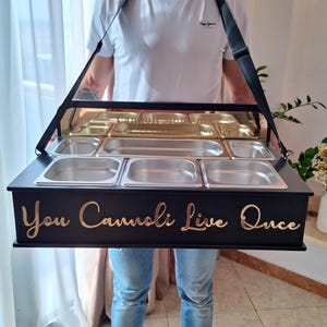 May include: A black serving tray with stainless steel containers and a clear top. The tray has a black strap for carrying and gold lettering that reads "You Cannoli Live Once".