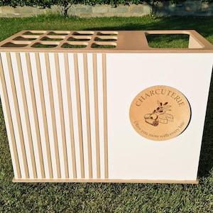 Puede incluir: Una estaci&oacute;n de servicio de charcuter&iacute;a blanca y de madera con un dise&ntilde;o de listones en un lado. La estaci&oacute;n presenta un letrero circular de madera que dice "Charcuter&iacute;a" con el texto "Olive you more with every bite."
