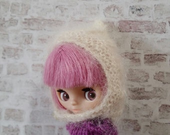 May include: A doll with pink hair wearing a white knitted hat and a purple knitted sweater.