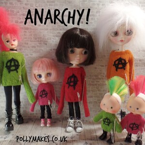 Könnte beinhalten: Fünf Puppen tragen bunte Pullover mit einem Anarchiesymbol. Die Puppen haben verschiedene Frisuren und sind in einer Reihe aufgestellt. Der Text "ANARCHY!" steht über den Puppen.