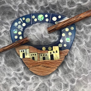 May include: A wooden knitting needle with a blue and white ceramic needle holder featuring a town skyline design. The needle holder has a circular opening for the needle to pass through.
