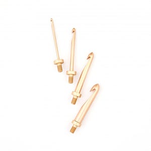 Könnte beinhalten: Vier goldfarbene Häkelnadeln in verschiedenen Größen sind auf weißem Hintergrund angeordnet. Jeder Haken hat einen Gewindesockel und ein gebogenes Hakenende. Die Haken sind für Handarbeiten mit Garn konzipiert und eignen sich für verschiedene Projekte.
