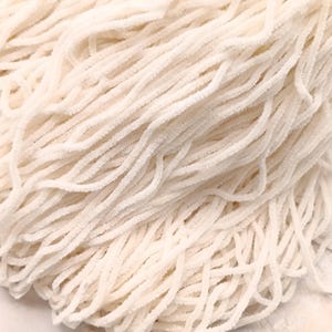 May include: Close-up of a pile of off-white chenille stems. The stems are soft, fuzzy, and arranged in a dense, intertwined pattern. The texture is visible, with each stem appearing slightly twisted. The overall effect is a soft, tactile, and inviting appearance.