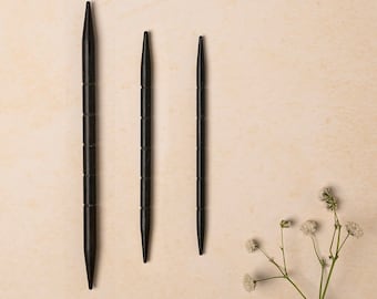 May include: Three black knitting needles of different sizes on a beige background.
