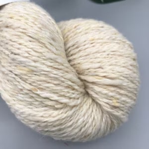 May include: A skein of cream-colored yarn with flecks of yellow throughout.
