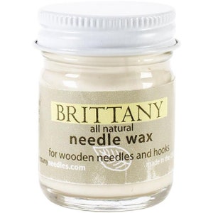 May include: A small white jar with a gold label that reads "Brittany all natural needle wax for wooden needles and hooks brittanyneedles.com made in the US".