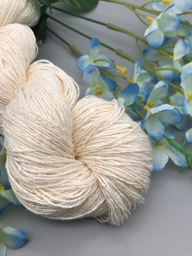 May include: A skein of natural white cotton yarn, perfect for knitting or crocheting. The yarn is soft and smooth, and it has a subtle sheen.