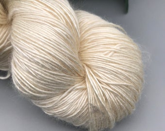 May include: A skein of off-white yarn, made from natural fibres, is shown against a grey background. The yarn is soft and fluffy, and it is ideal for knitting or crocheting.