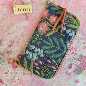 May include: A rectangular zippered pouch featuring a dark navy fabric base with multi-colored floral and botanical embroidery in shades of pink, green, and blue. The pouch includes tan leather-like trim and a matching zipper pull with an Atenti tag.