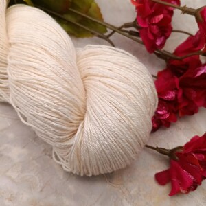 May include: A skein of off-white yarn, likely cotton, with a soft, natural texture. The yarn is loosely wound and has a subtle sheen.