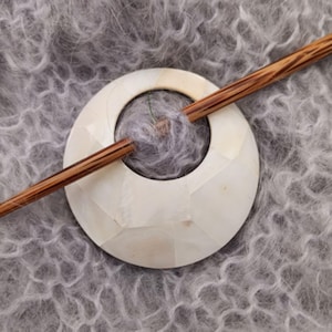 Peut inclure: Un fuseau en bois reposant sur un fuseau en bois blanc rond et décoratif. Le fuseau a une surface texturée et un trou au centre. Le fuseau est en bois avec des rayures brunes et blanches.