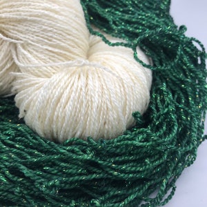 May include: Two skeins of yarn, one white and one green with gold glitter. The white yarn is in a ball shape and the green yarn is loose.