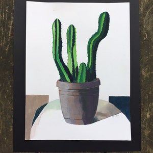 May include: A watercolor painting of a cactus in a brown pot. The cactus has green and dark green vertical stripes. The pot sits on a white surface with geometric shapes in the background. The artwork is framed in a black mat.