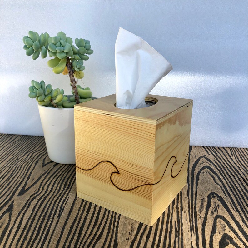 Pode incluir: Uma caixa de len&ccedil;os de papel de madeira com um design de ondas. A caixa &eacute; feita de madeira clara e tem um acabamento natural. O design de ondas &eacute; esculpido na madeira e &eacute; de cor castanho escuro.