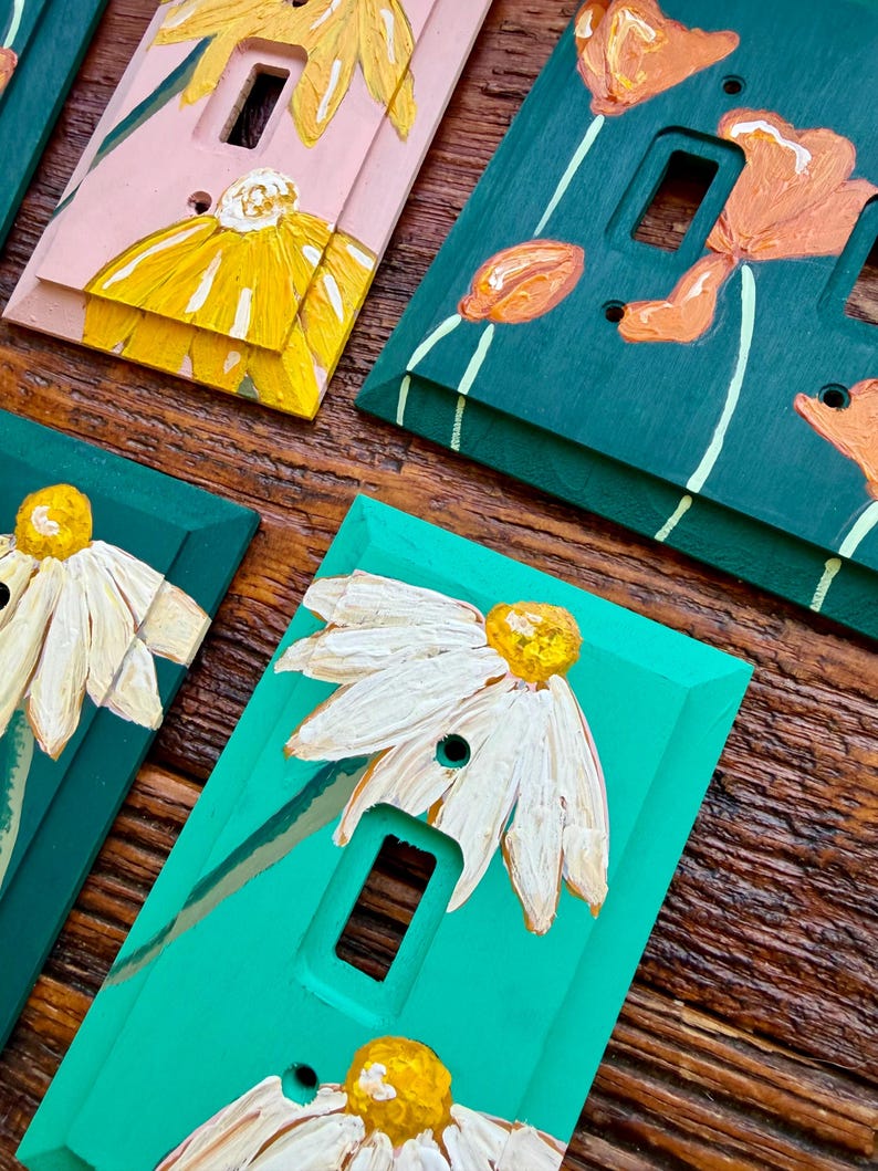 K&ouml;nnte beinhalten: Eine Sammlung rechteckiger Lichtschalterabdeckungen mit handgemalten Blumenmotiven. Die Abdeckungen sind in verschiedenen Farben wie Rosa, Dunkelgr&uuml;n und leuchtendem T&uuml;rkis gehalten und mit strukturierten gelben, orangen oder wei&szlig;en Blumen verziert.