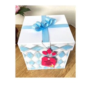 May include: A white gift box with a blue ribbon and bow. The box has a blue and white checkered pattern on the bottom and a pink tag with the text "Happy Anniversary! Have a great time!"