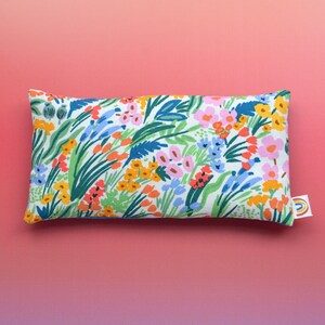 May include: A white pillow with a floral print featuring a variety of colorful flowers and green leaves. The pillow is rectangular and has a white background.