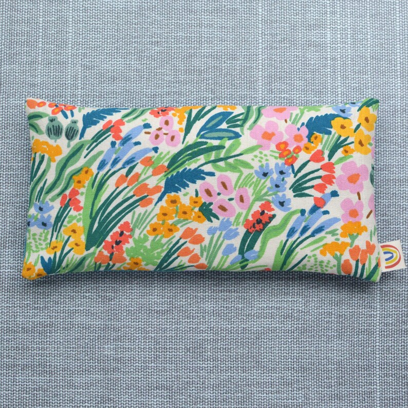 May include: A rectangular floral print eye pillow with a white background and a variety of colorful flowers and leaves. The pillow is made of soft fabric and is perfect for relaxation and sleep.