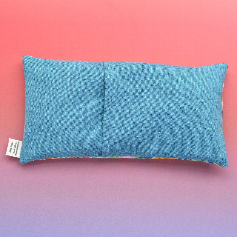 May include: A blue linen eye pillow with a floral print on the back. The pillow has a seam down the center and a small white tag with the text "Made with love in California".