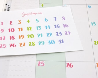 Könnte beinhalten: Ein Blatt mit bunten Zahlenaufklebern für einen Kalender. Die Zahlen sind in einem Regenbogen-Farbverlauf von Pink bis Lila. Die Zahlen sind von 1 bis 31. Das Blatt liegt auf einem Kalender mit dem sichtbaren Monat Oktober.