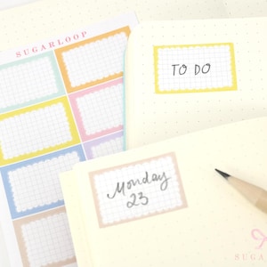 Peut inclure: Une planche d'autocollants rectangulaires aux bords festonnés dans des tons pastel comme le jaune, le bleu, le rose et le vert, avec un motif quadrillé. Certains sont collés sur un carnet à points avec le texte manuscrit TO DO et Monday 23.