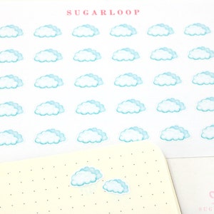 May include: Sheet of cloud stickers with a light blue and white design. The word "SUGARLOOP" is printed in pink at the top. A dotted notebook is in the foreground with two cloud stickers.