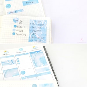 May include: A blue and white watercolor planner with a weekly spread. The planner has a tabbed section for each month of the year. The planner also includes a section for goals and to-do lists. The planner is decorated with blue and white watercolor stickers.