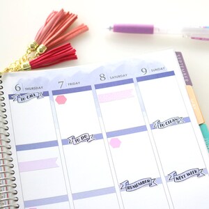 May include: A close-up of a planner with a silver coil binding. The planner has a light blue background with white and pink stickers. The stickers have text that reads "To Call", "To Do", "To Clean", "Remember", and "Next Week".