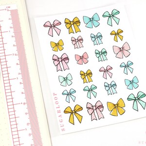 May include: A sheet of colorful bow stickers with a variety of pastel colors, including pink, blue, yellow, and green. The stickers are arranged in rows and columns on a white background. The sheet is labeled "Sugarloop" in the bottom left corner.
