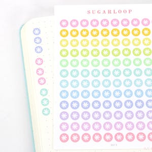 May include: A sheet of rainbow colored stickers with a white snowflake design. The stickers are arranged in rows and columns on a white background. The sheet is labeled "SUGARLOOP".