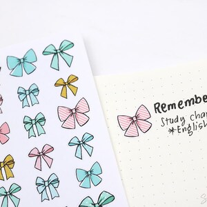 May include: A sheet of colorful bow stickers with a pink, blue, and yellow color scheme. The stickers are arranged in a grid pattern. The sheet is next to a white page with black text that reads "Remember Study chapters *English*"