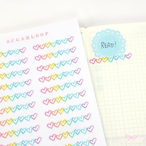 May include: A sheet of rainbow heart stickers with the text "SUGARLOOP" at the top. The stickers are arranged in rows of 10 hearts each, with each heart outlined in white and filled with a different colour of the rainbow. The stickers are on a white background.