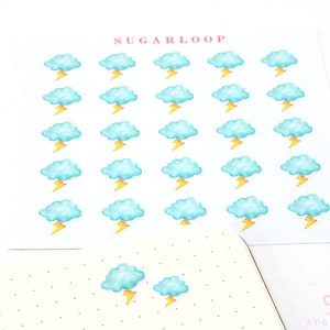 Puede incluir: Una hoja de pegatinas con 36 nubes azules con rayos amarillos. La hoja es blanca con el texto "SUGARLOOP" en la parte superior.
