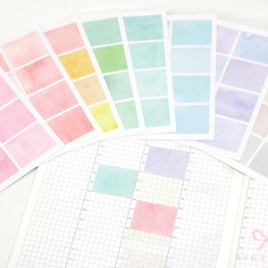 May include: A collection of rectangular sticker sheets featuring watercolour gradients in pink, orange, yellow, green, blue, purple, and neutral tones, arranged in a fan shape above a grid-lined planner page with some stickers applied.