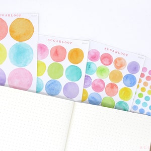 Könnte beinhalten: Vier Blätter mit bunten Aquarell-Punkt-Stickern. Jedes Blatt zeigt einen anderen Farbverlauf von Punkten, von hell bis dunkel. Die Blätter sind mit "Sugarloop" beschriftet und haben einen weißen Hintergrund.