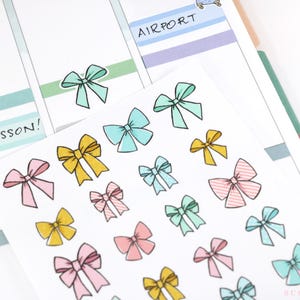 May include: A sheet of colorful bow stickers with a variety of colors including pink, yellow, blue, and green. The stickers are arranged in rows on a white background. The text "PIANO LESSON!" is written on the sheet.